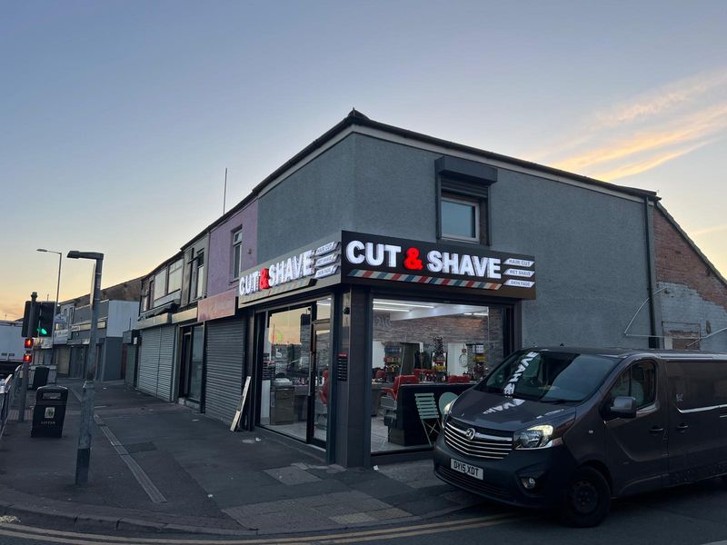 Cut & Shave barbers corner shopfront illuminated at dusk