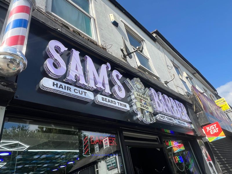 Illuminated Sam's Barbers shopfront with traditional barber pole