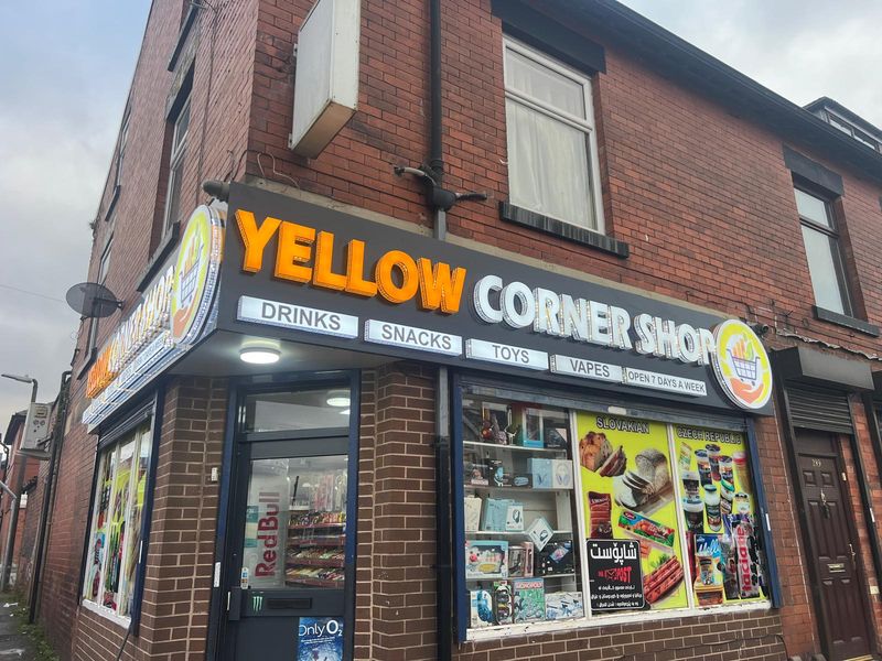 Yellow and green illuminated corner shop fascia sign